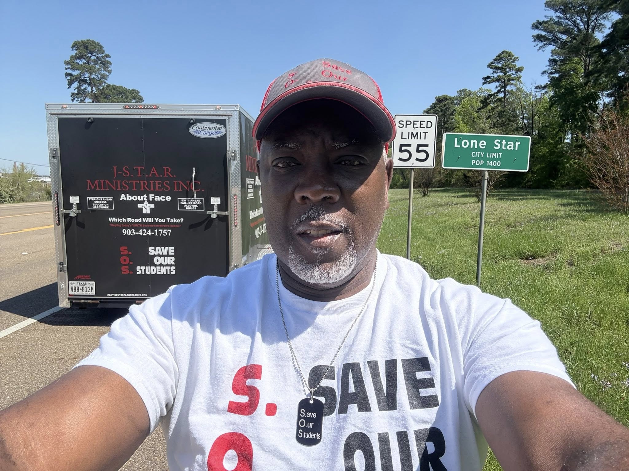 Patrick beside the Lone Star city limit sign, with the J-STAR relief trailer behind him.